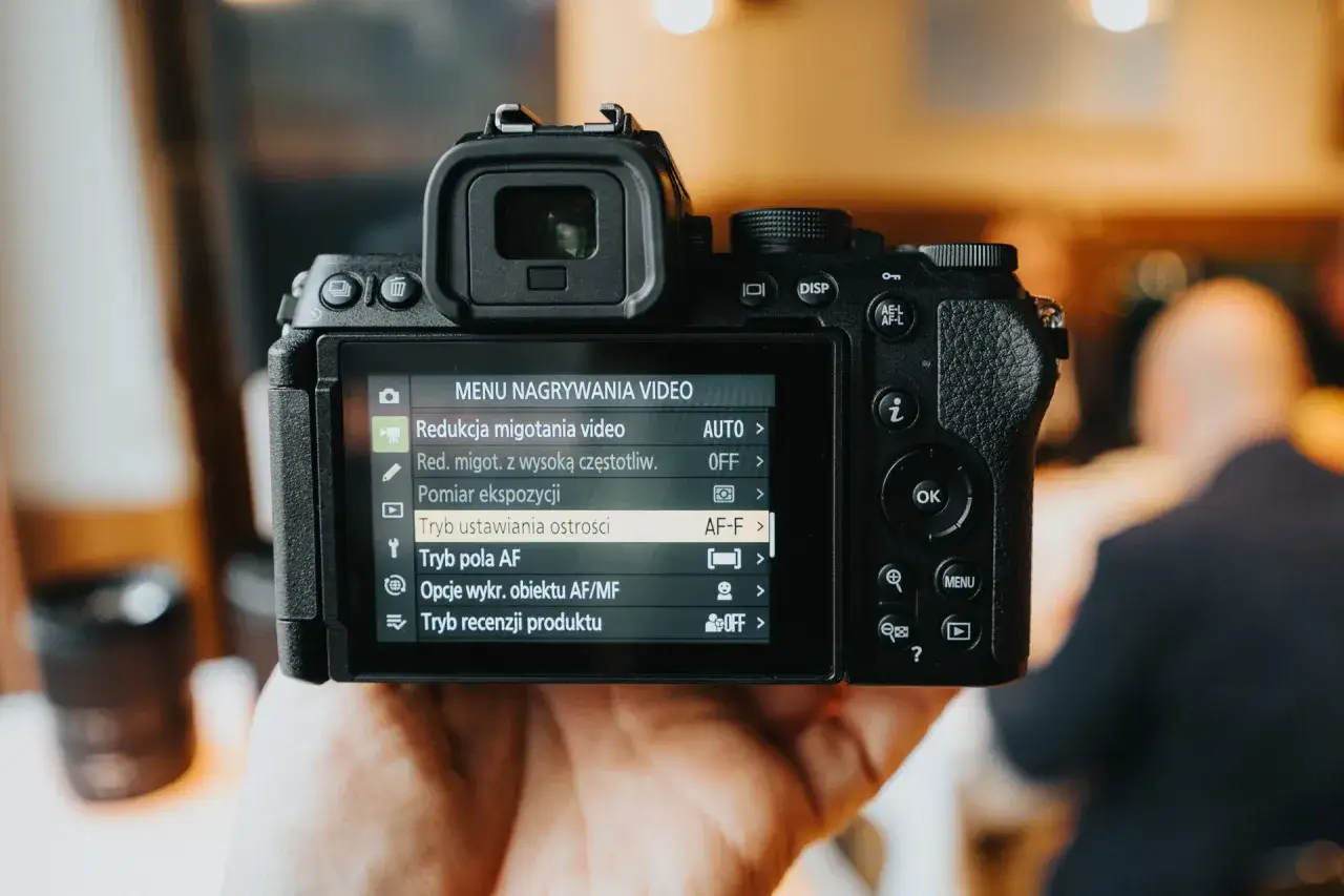 Dłoń trzyma aparat lustrzanka nikon, na ekranie widoczne menu nagrywania wideo z opcją 