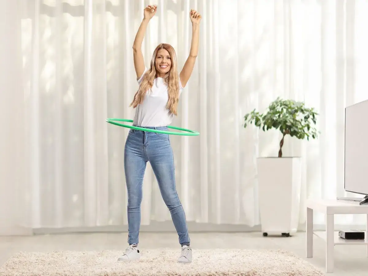 Uśmiechnięta kobieta kręci zieloną obręczą, zastanawiając się, czy hula hop odchudza.
