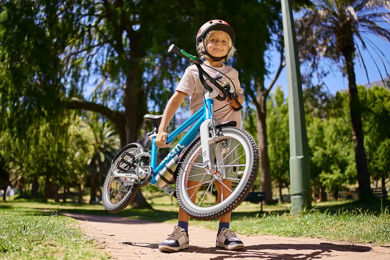 Chłopiec w kasku trzyma lekki, niebieski rower. Idealny, by dowiedzieć się, ile powinien ważyć rower dla 4 latka.