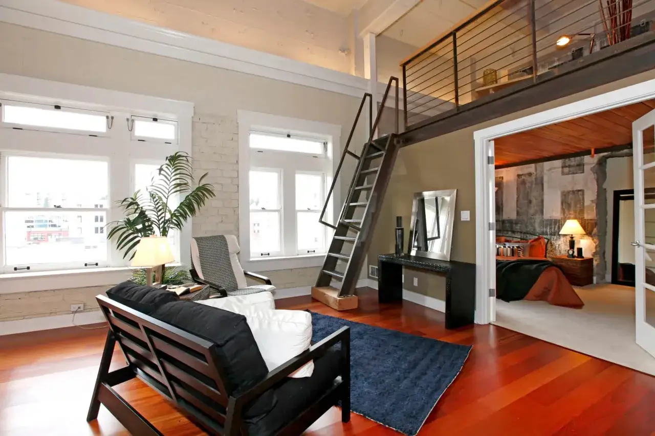 Nowoczesna antresola w domu z metalową klatką schodową, widok na sypialnię i salon z czarną sofą.