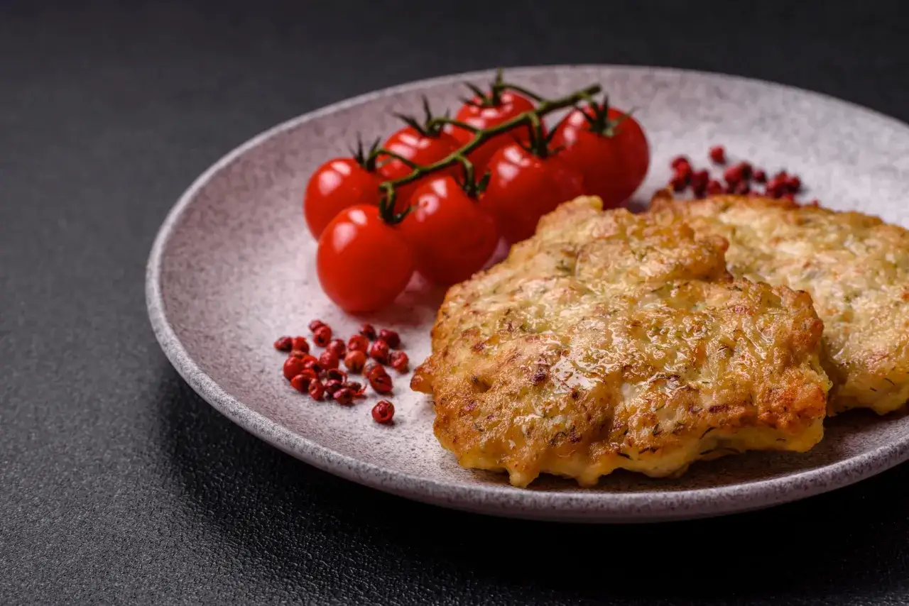 Złociste kotlety schabowe na talerzu z pomidorkami i pieprzem. Sekret jak usmażyć schabowego żeby panierka nie odpadała na patelni.