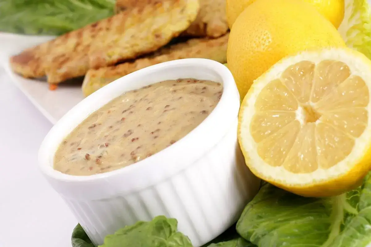 Sos musztardowy z ziarnami gorczycy, podany z cytryną i sałatą, idealny do panierowanych kawałk&oacute;w kurczaka.