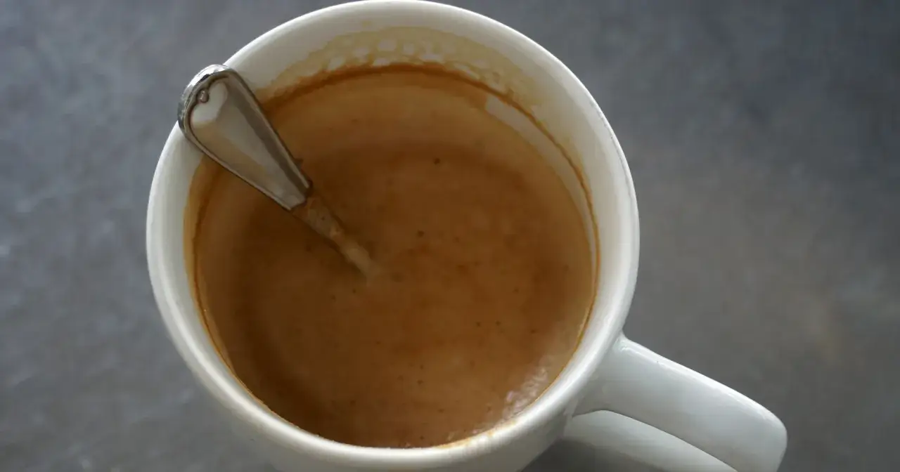 Kawa w białym kubku z łyżeczką. Czy kawa szkodzi na wątrobę? Badania sugerują, że umiarkowane spożycie kawy może być korzystne dla wątroby.