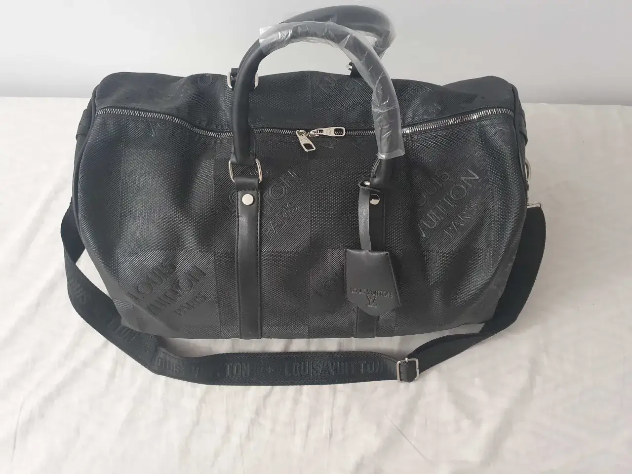 Elegancka, duża torebka Louis Vuitton w kolorze czarnym, z wytłoczonym monogramem i paskiem na ramię. Idealna na podróż.
