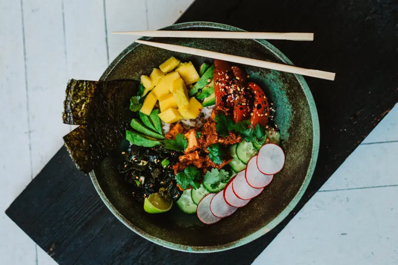 Kolorowa miska pełna zdrowych składnik&oacute;w: ryż, awokado, mango, og&oacute;rek, rzodkiewka, wodorosty i pieczona papryka. Idealna odpowiedź na pytanie: dieta wegańska co jeść.