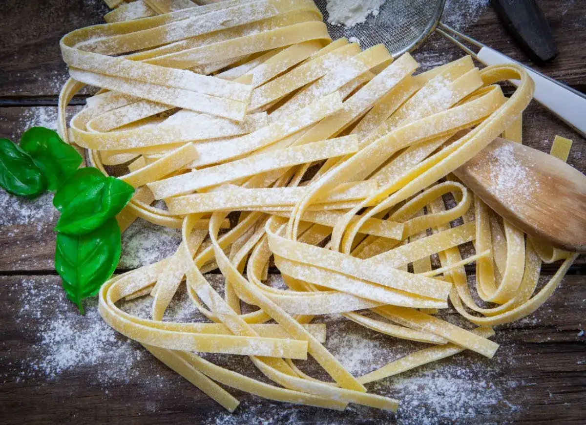 Świeży, jajeczny makaron bezglutenowy, gotowy do przygotowania według przepisu. Obok listki bazylii i drewniana łyżka.