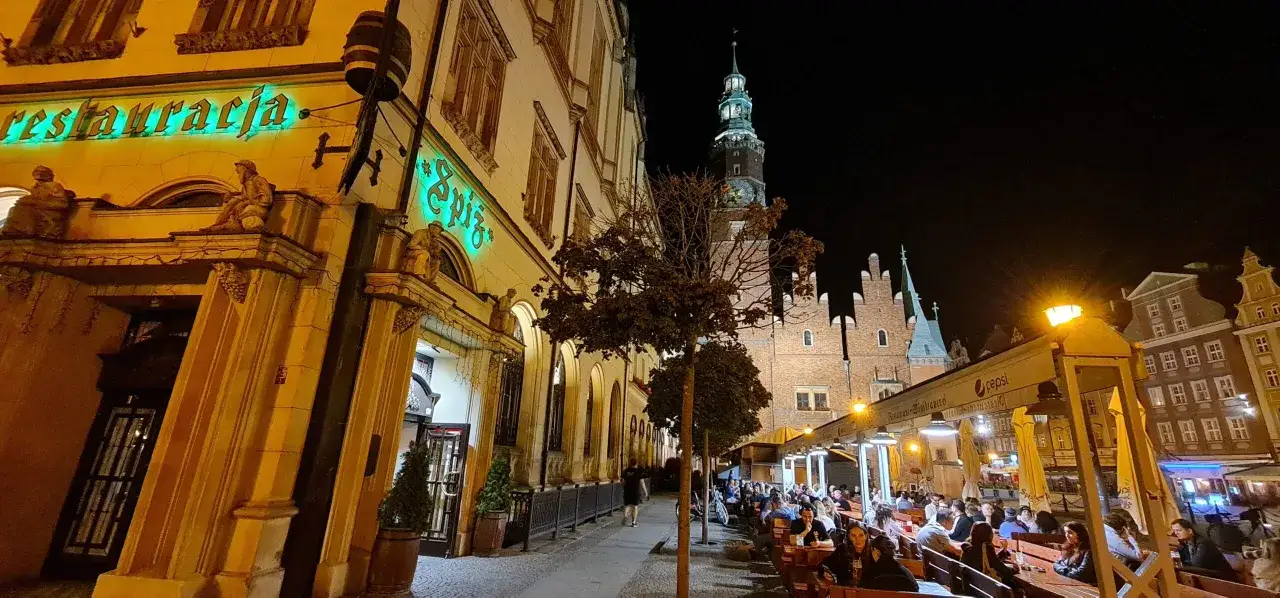 Wieczorny Wrocław tętni życiem. Restauracje i ogr&oacute;dki piwne pełne ludzi, idealne wrocławskie atrakcje dla dorosłych. W tle widać Ratusz.