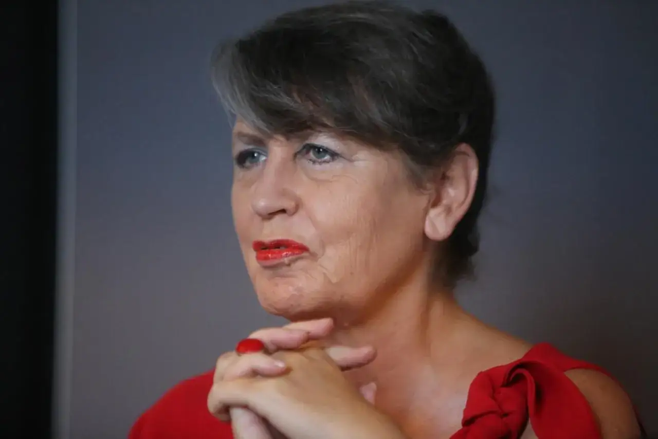 Joanna Wnuk Nazarowa w czerwonej sukience, z dłońmi złożonymi na piersi i wyrazistą czerwoną szminką.
