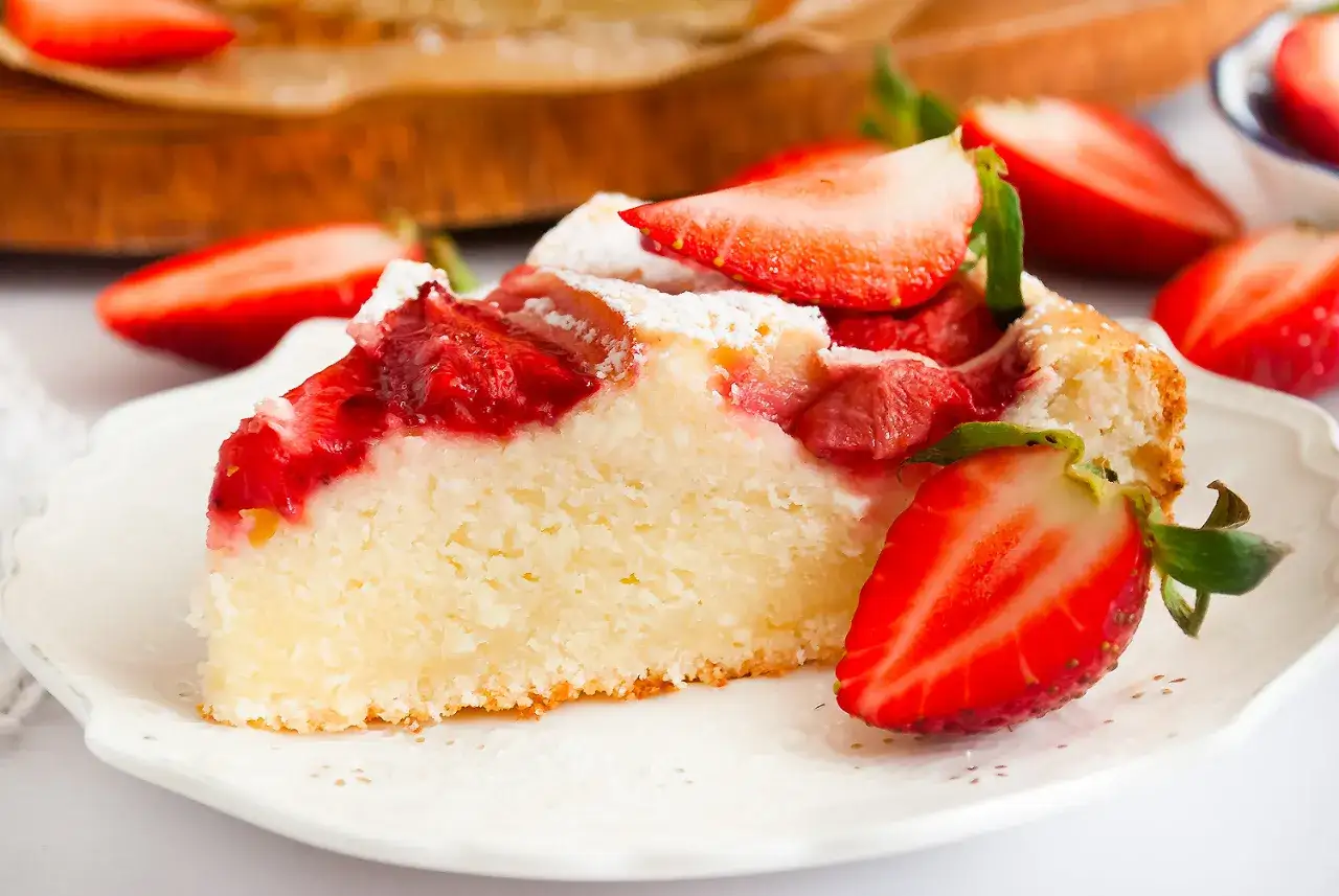 Szybkie ciasto z twarogiem i truskawkami, posypane cukrem pudrem, na białym talerzyku.