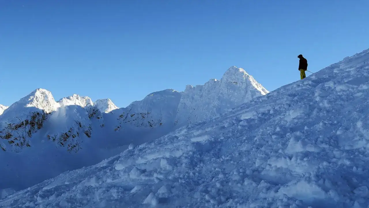 Narciarz na ośnieżonym stoku g&oacute;rskim. Czy szlaki turystyczne są otwarte? Słońce oświetla szczyty, a niebo jest błękitne.