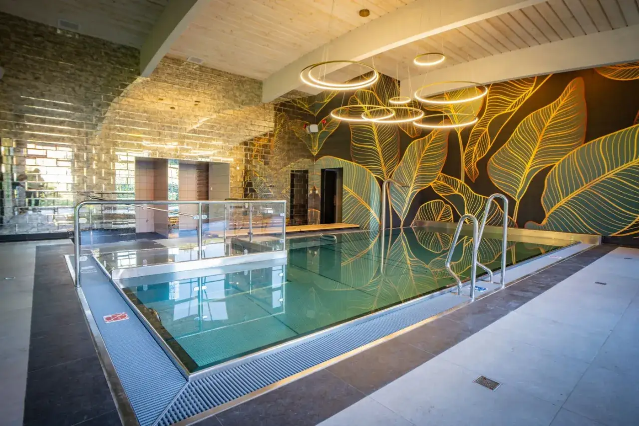 Nowoczesny basen w spa Białystok i okolice. Ściana z motywem liści, lustrzana ściana i designerskie oświetlenie tworzą relaksującą atmosferę.