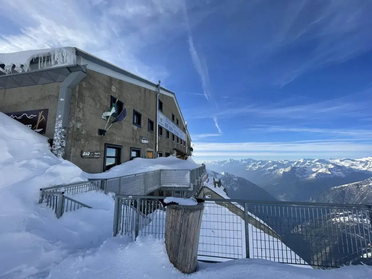 Zimowy krajobraz na szczycie Mont Blanc. Schronisko Rifugio Torino zasypane śniegiem, z lodowymi sopelkami zwisającymi z dachu. W tle rozciągają się ośnieżone szczyty Alp.