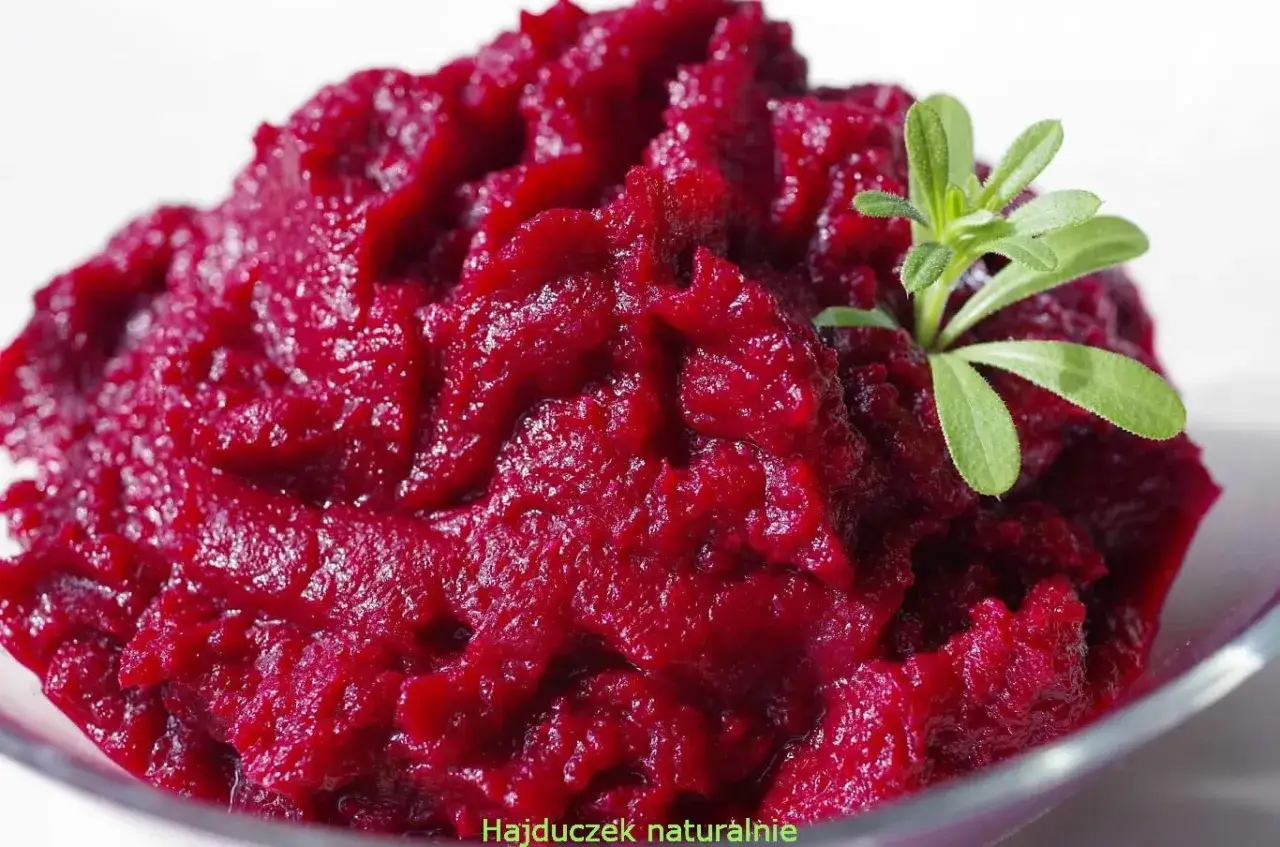 Intensywnie czerwone buraczki z chrzanem, podane w szklanej miseczce, ozdobione gałązką zielonej roślinki.