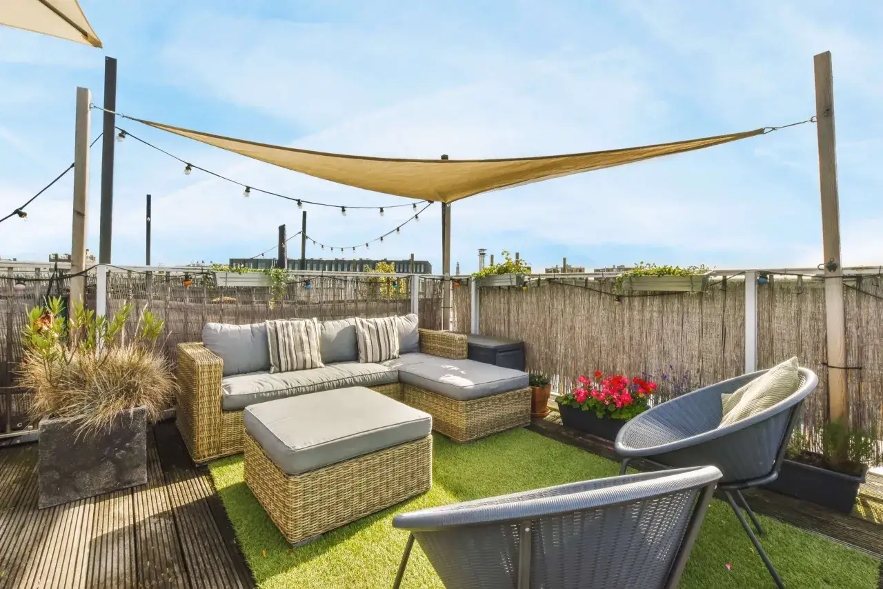 Jak zamontować żagiel na tarasie? Widok na taras z meblami rattanowymi, sztuczną trawą i żaglem przeciwsłonecznym.