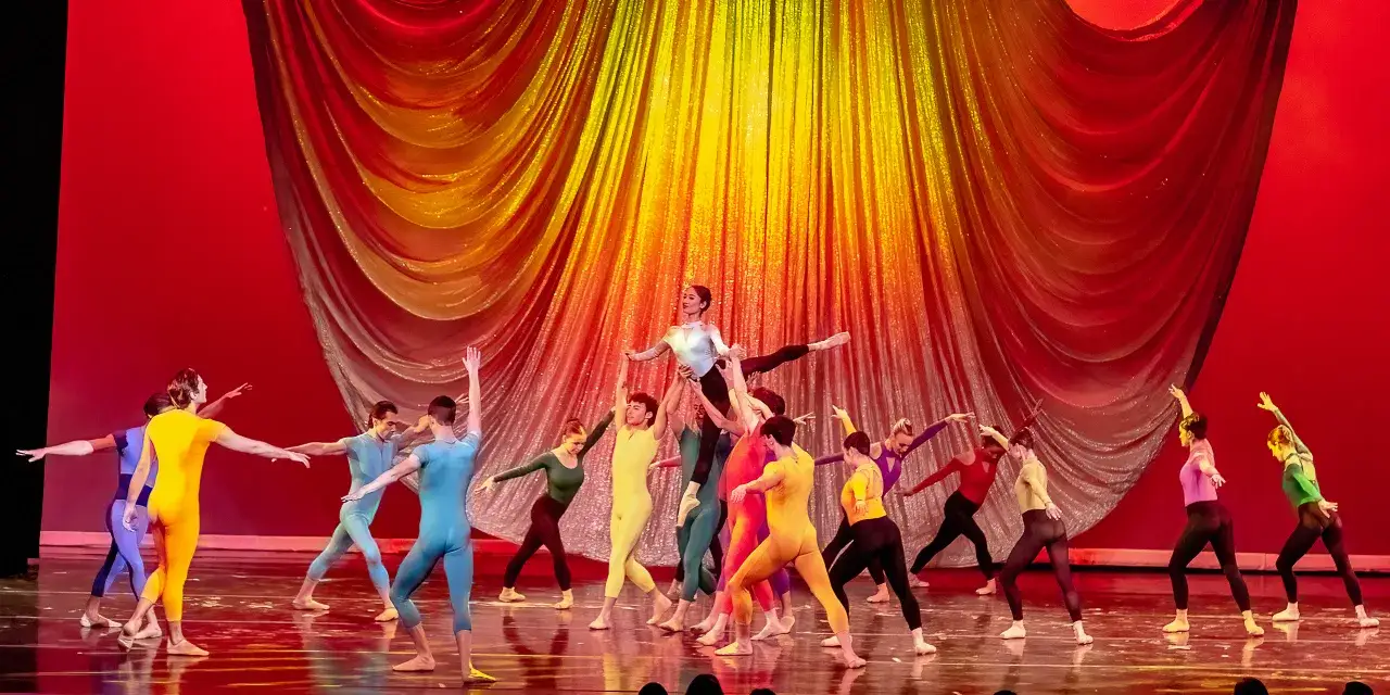 Tancerze w barwnych strojach wykonują dynamiczne układy na scenie, tworząc żywiołową wizję inspirowaną 