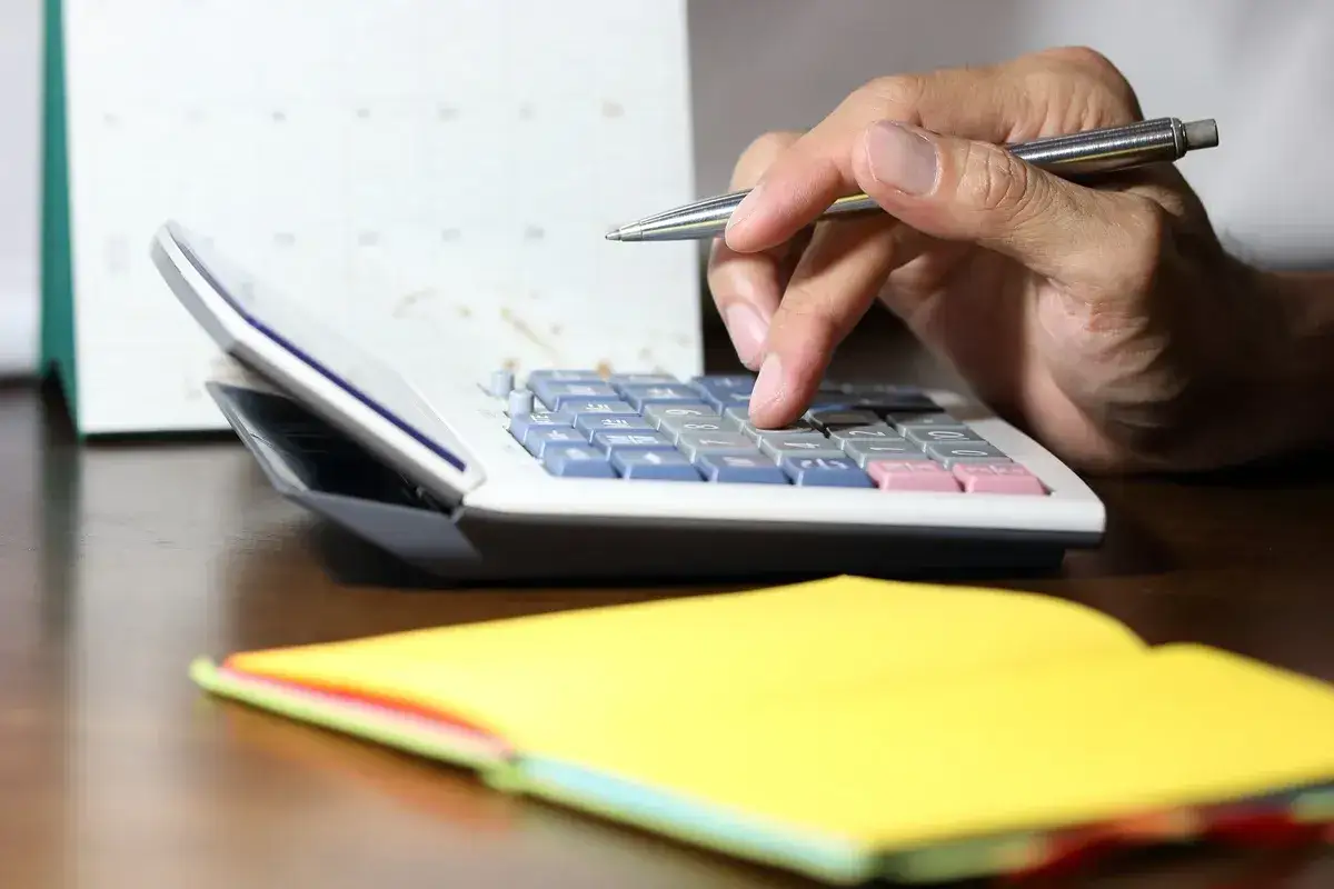 Dłoń z długopisem liczy na kalkulatorze, obok żółty notatnik. Czy krus wlicza się do stażu pracy w budżetówce?