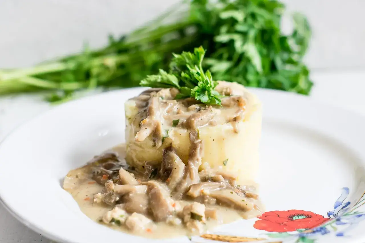 Puszysty ziemniak polany kremowym sosem z boczniak&oacute;w, udekorowany natką pietruszki.