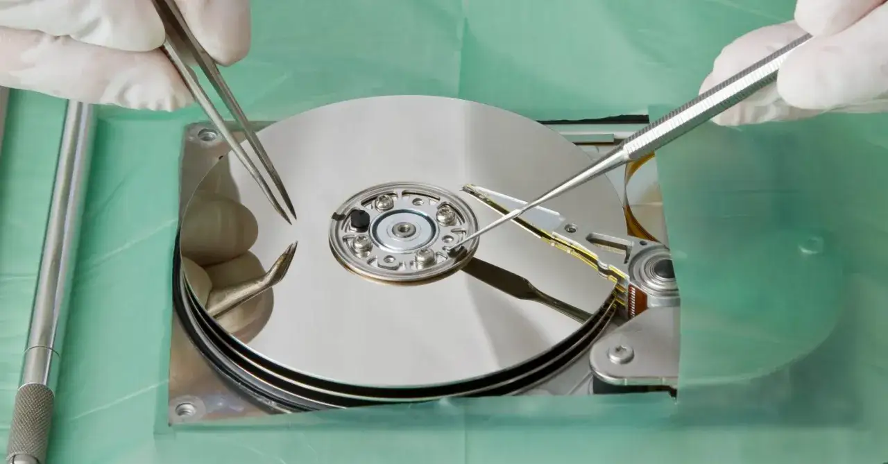 Precyzyjna praca przy dysku twardym, gdzie narzędzia chirurgiczne dotykają błyszczących talerzy, niczym kryształowe dyski, w celu odzyskania danych.