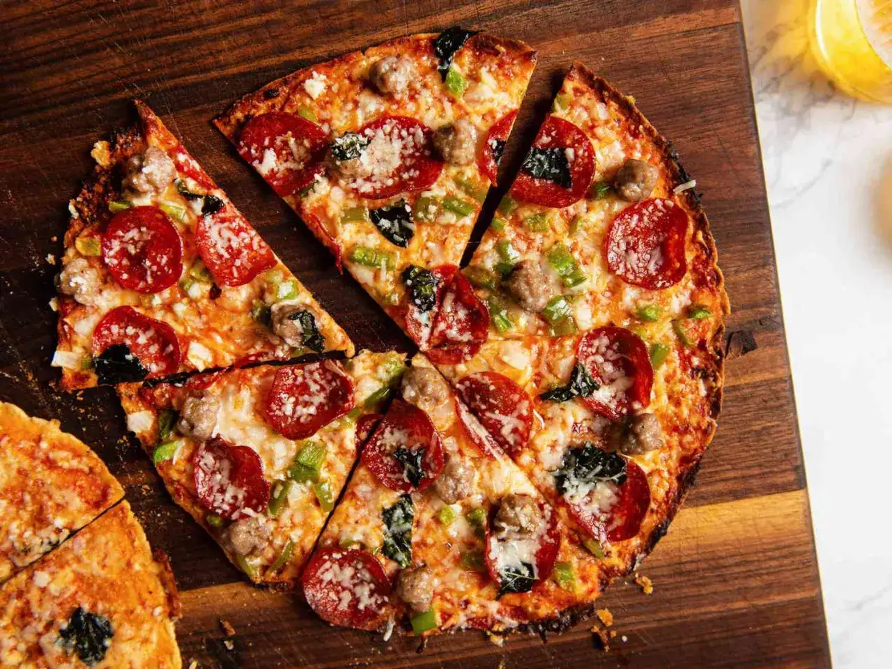 Chrupiąca pizza z tortilli z pepperoni, kiełbasą i zieloną papryką, pokrojona na kawałki, leży na drewnianej desce.