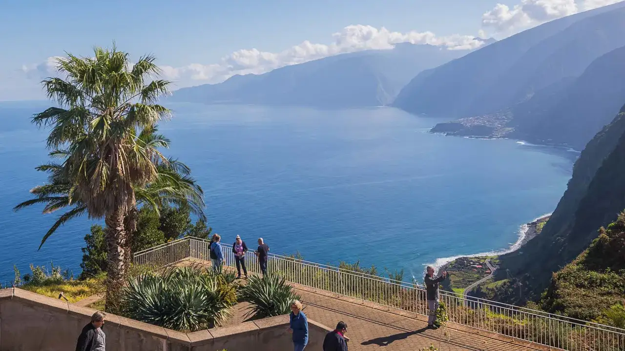 Widok na ocean i góry na Maderze. W lutym panuje tu przyjemna temperatura, idealna na spacer po tarasie widokowym z palmami.