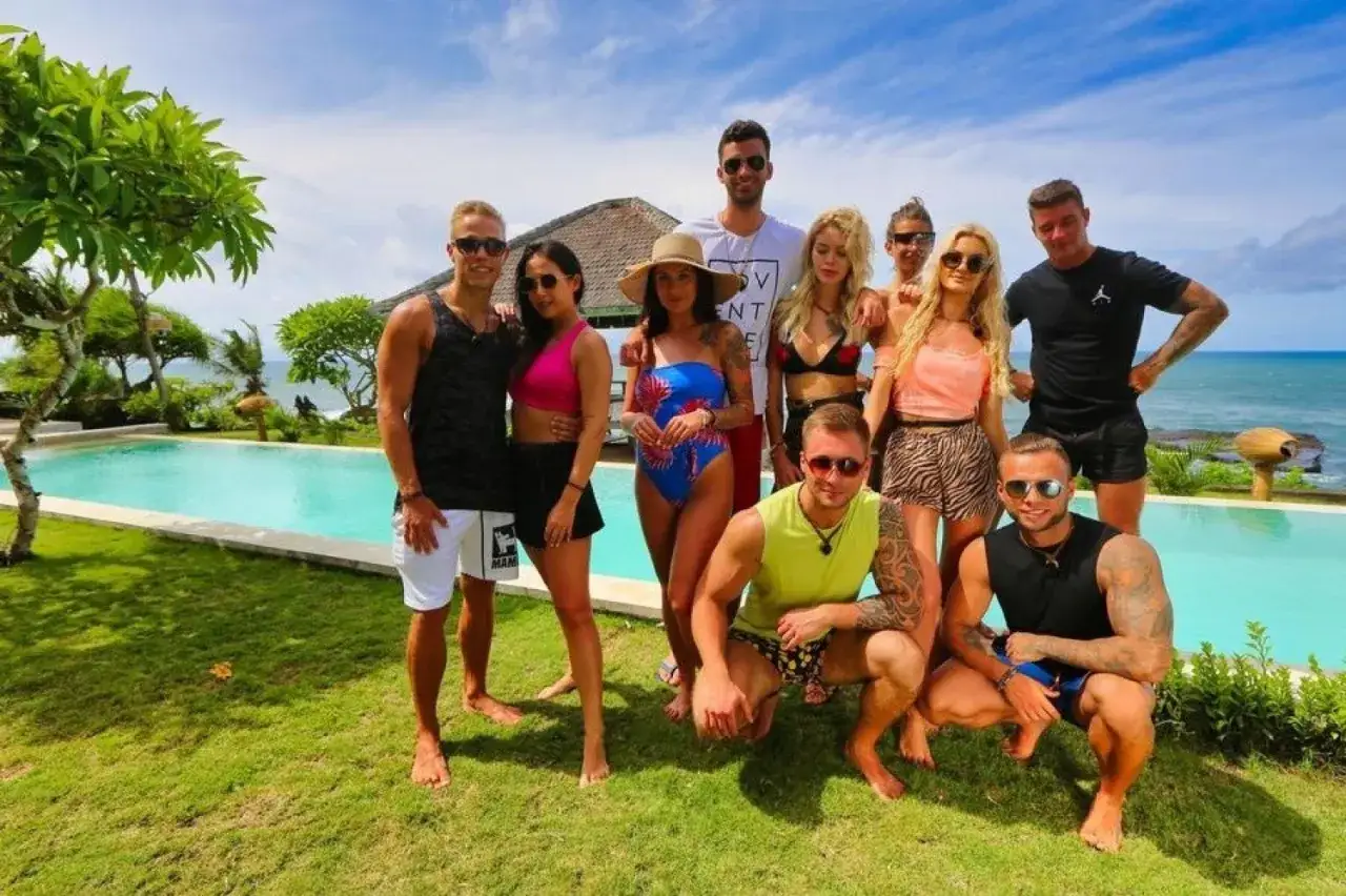 Uczestnicy Hotel Paradise 1 pozują do zdjęcia na tle basenu i oceanu.
