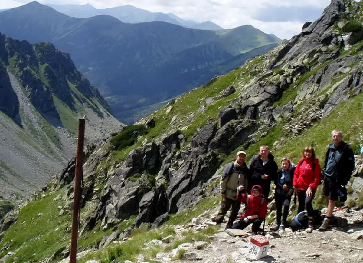 Grupa turyst&oacute;w na szlaku w Tatrach, w tle majestatyczne g&oacute;ry. Wrota Chałubińskiego w oddali.