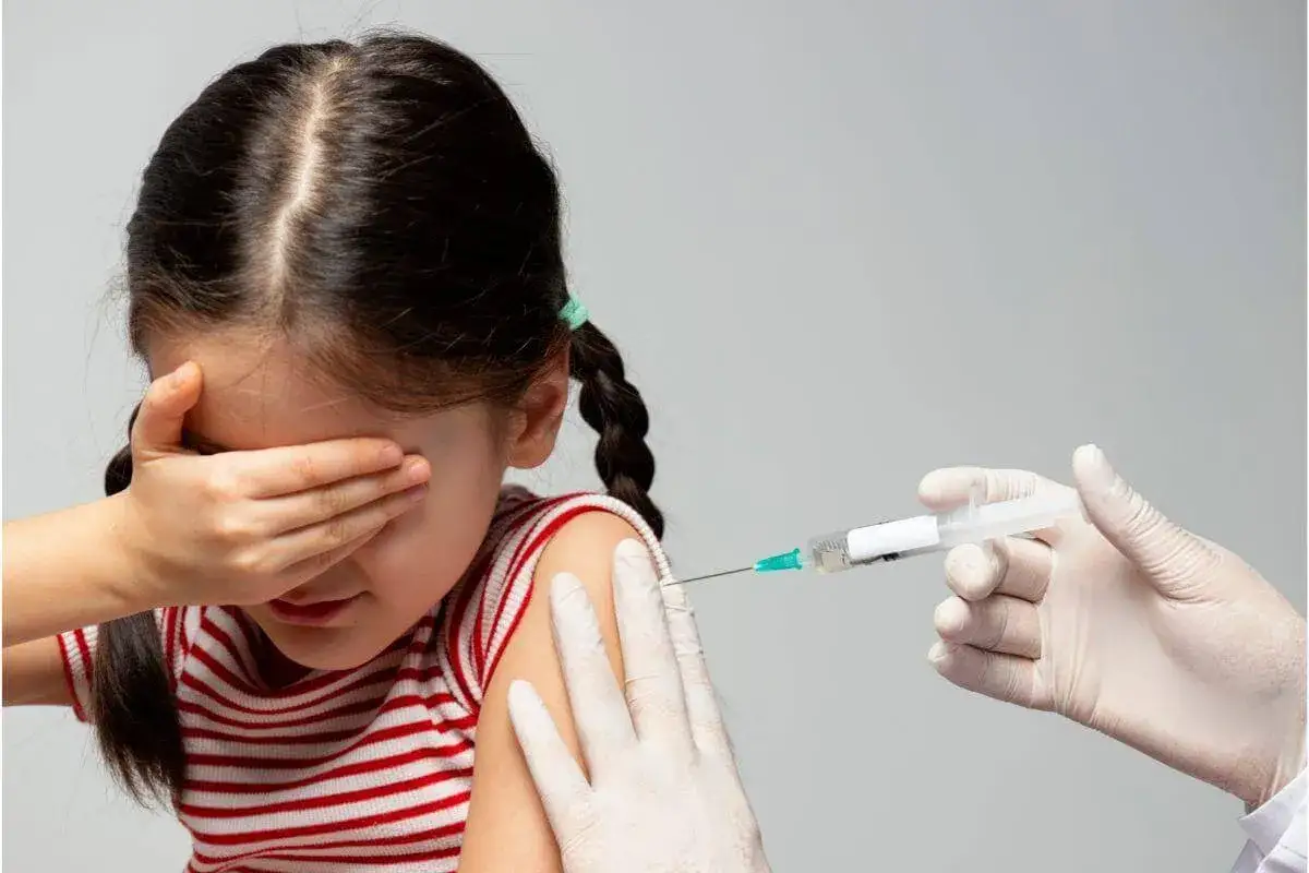 Dziewczynka zamyka oczy przed zastrzykiem. Jak leczyć hemofobię? Wsparcie i rozmowa pomagają pokonać strach przed igłą.