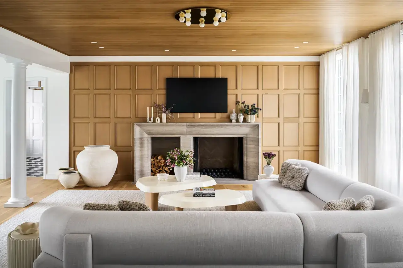 Nowoczesna metamorfoza starej boazerii w salonie. Drewniane panele tworzą ciepłe tło dla kamiennego kominka i jasnej sofy.