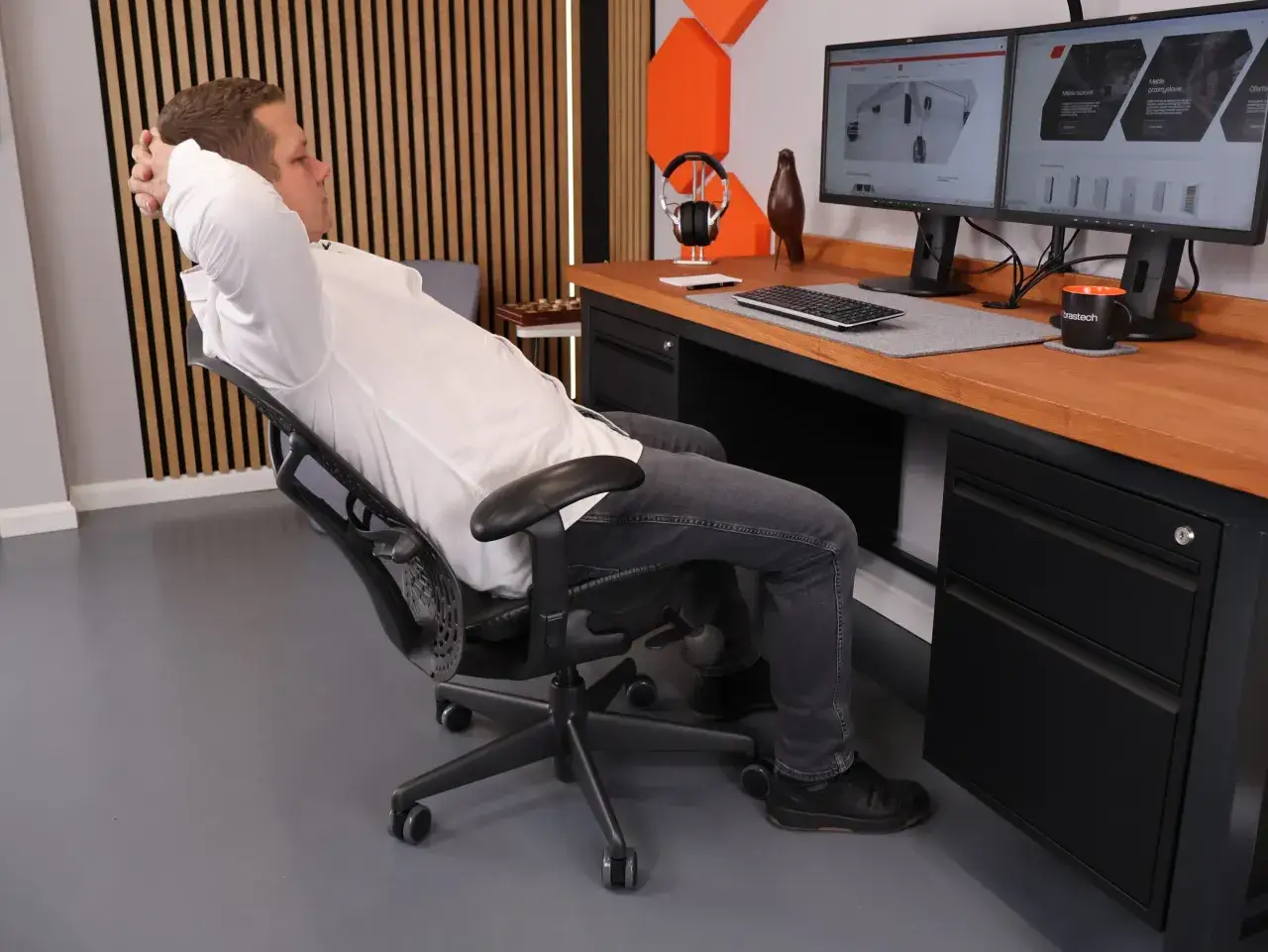 Mężczyzna odpoczywa przy biurku z dwoma monitorami. Wymiary biurka są idealne do pracy i relaksu.