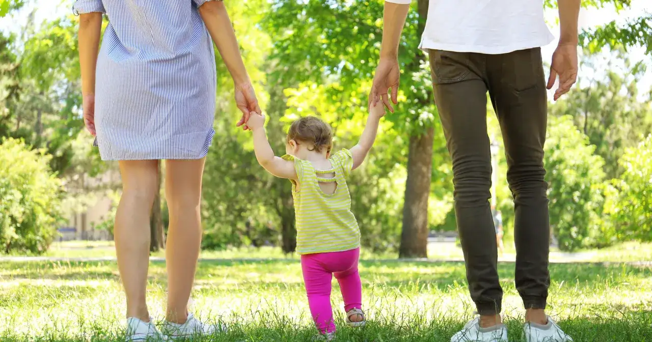 Rodzice trzymają za ręce dziecko, które stawia pierwsze kroki. Po kim dziecko dziedziczy inteligencję? To pytanie, na które odpowiedź kryje się w genach.