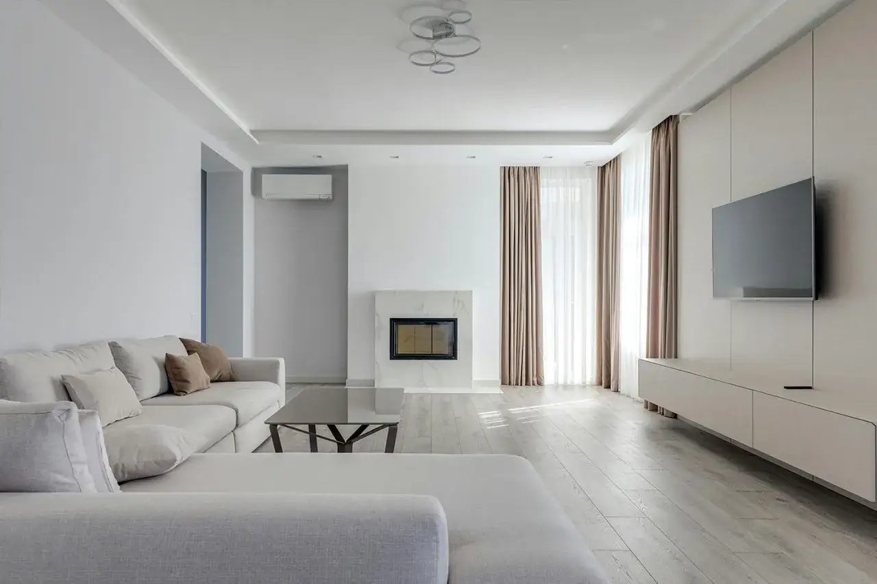 Jasne, nowoczesne firany w salonie tworzą przytulną atmosferę. Wygodna kanapa, kominek i telewizor zapraszają do relaksu.