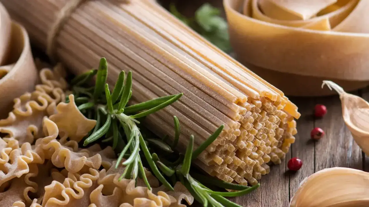 Jasny vs ciemny makaron: spaghetti, faliste kształty, rozmaryn i czosnek na drewnianym tle.