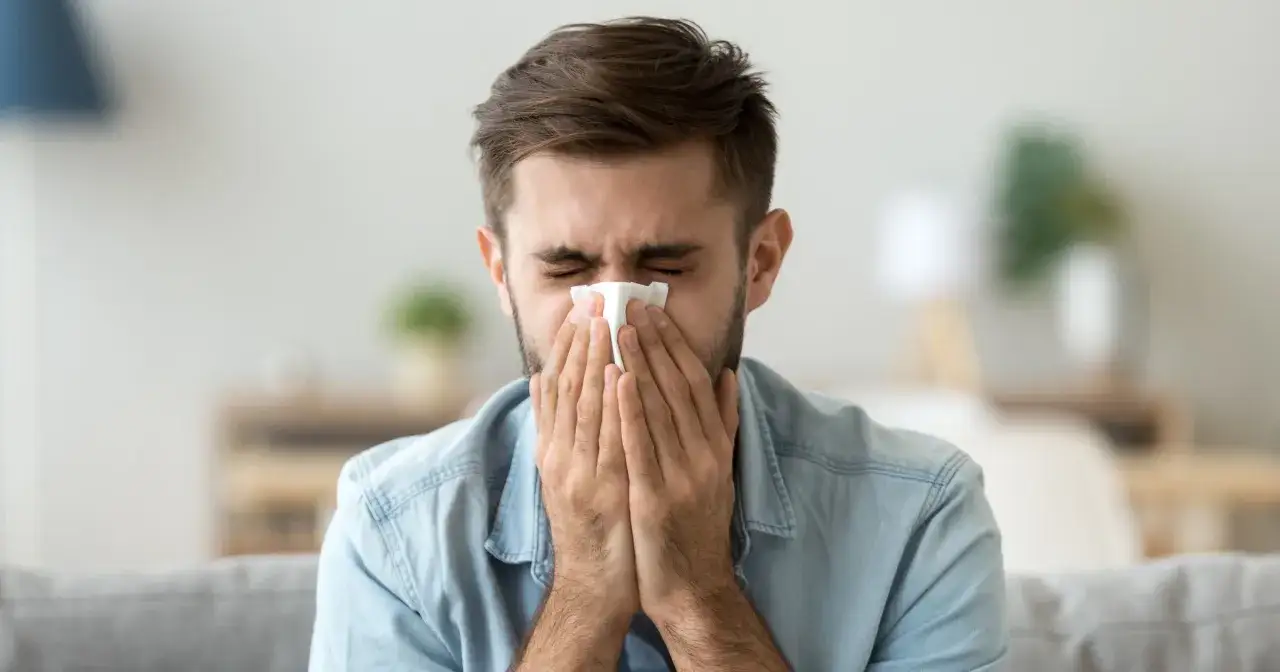 Mężczyzna z zamkniętymi oczami chusteczką wyciera nos, cierpiąc na katar z krwią.