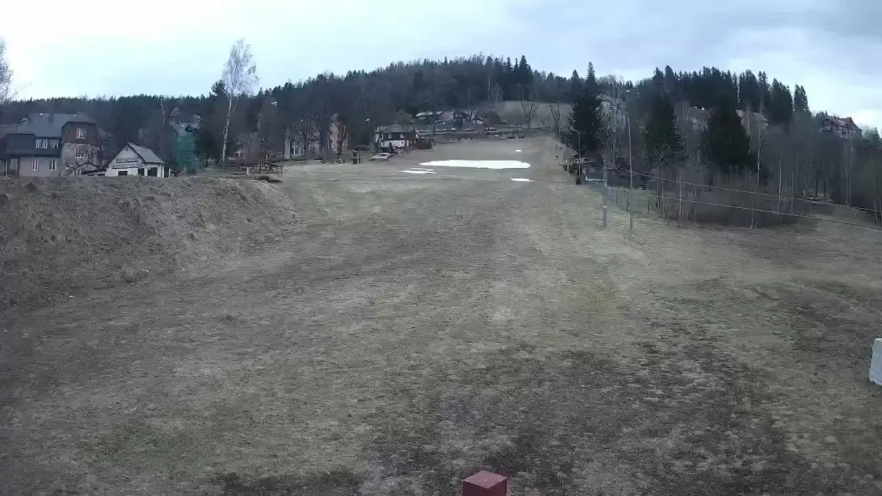 Stok Maciuś w Karpaczu, z widokiem na domy i las. Wiosna, śnieg topnieje.