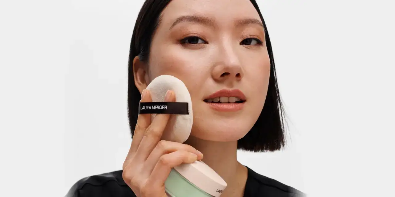 Kobieta pokazuje, jak nakładać puder sypki za pomocą puszka z logo Laura Mercier.