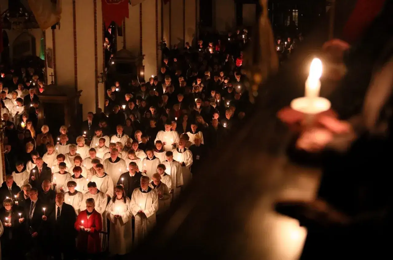 Uczestnicy procesji z zapalonymi świecami w kościele. Długość Wigilii Paschalnej zależy od tradycji i obrzędów.