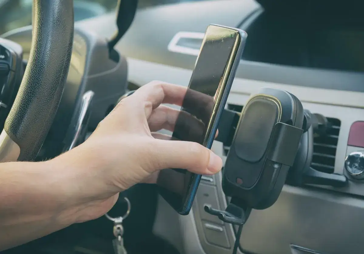 Dłoń wyjmuje telefon z uchwytu samochodowego. Uważaj na korzystanie z telefonu podczas jazdy.