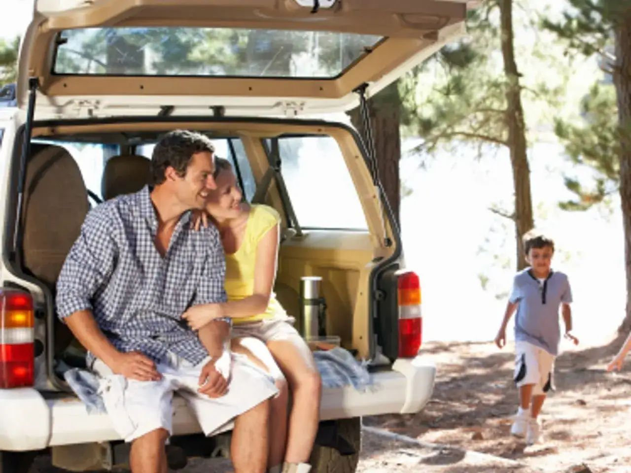 Para na tylnym siedzeniu samochodu, gotowi na piknik. W tle chłopiec biegnie przez las. Idealne jedzenie na podr&oacute;ż.