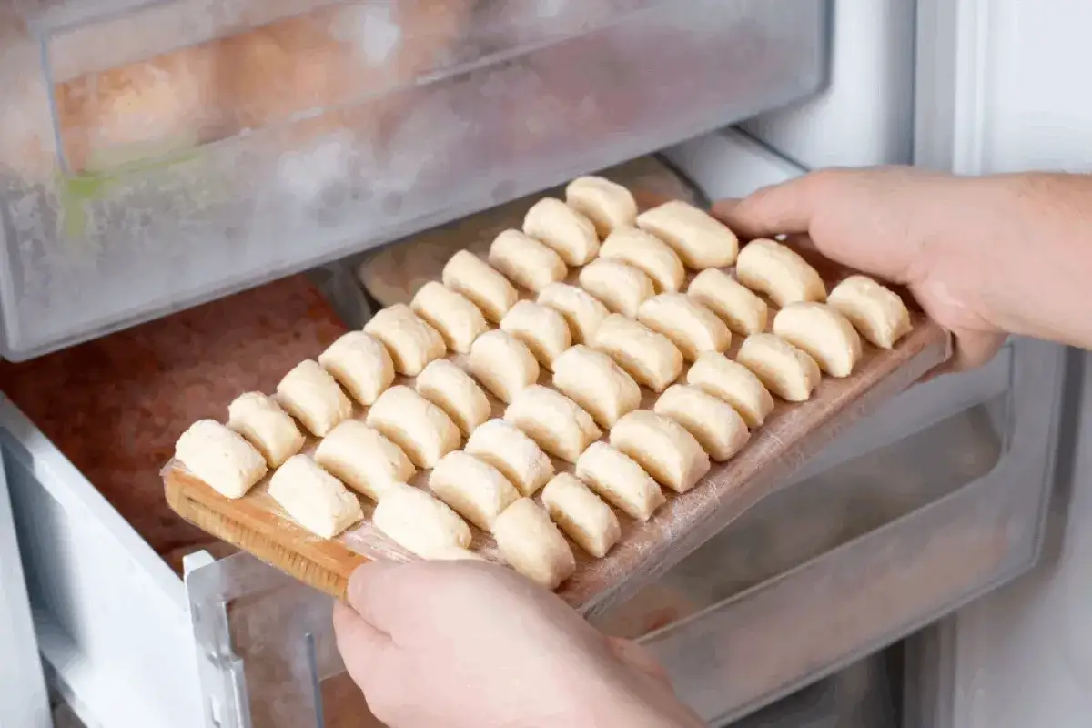 Ręce wkładają deskę z pierogami do zamrażarki. To prosty sposób, jak mrozić pierogi, by mieć je zawsze pod ręką.