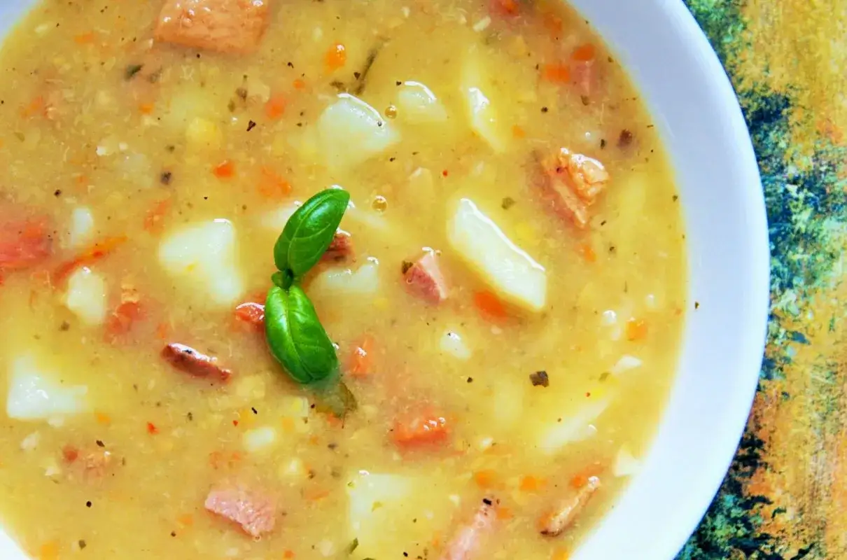 Gęsta grochówka wojskowa z ziemniakami i kawałkami mięsa, ozdobiona listkami bazylii. Czy to zupa soczewicowa?