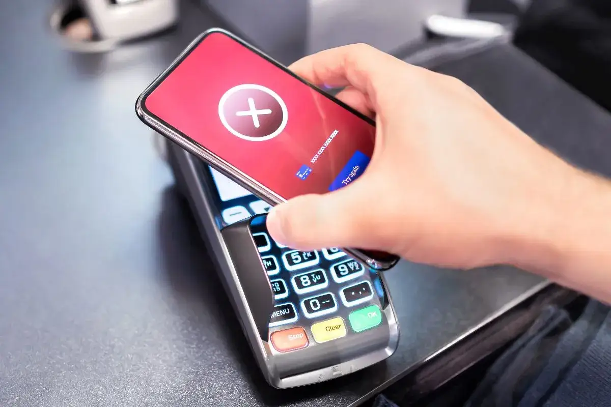 Dłoń zbliża telefon do terminala płatniczego. Na ekranie telefonu widnieje czerwony komunikat z krzyżykiem. Czy Vivigo można splacić na raty?