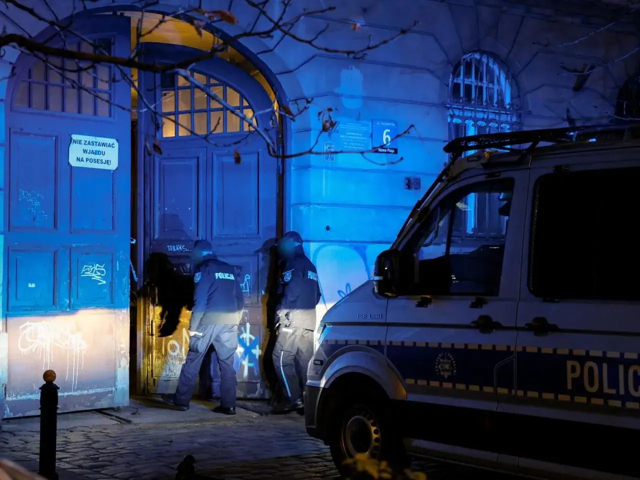 Nocna interwencja policji w domu znanej pary celebrytów. Funkcjonariusze wchodzą do kamienicy, obok stoi radiowóz.