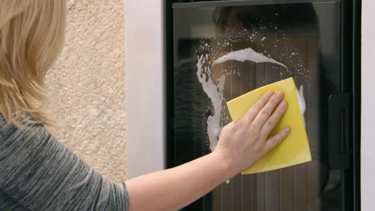 Kobieta czyści szybę kominka, używając żółtej gąbki i piany. Dowiedz się, jak wyczyścić kominek z piaskowca.