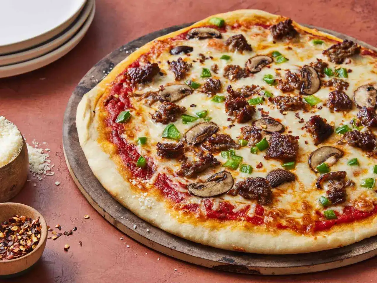 Pyszna pizza na cienkim cieście z mielonym mięsem, pieczarkami i zieloną papryką, posypana płatkami chili.