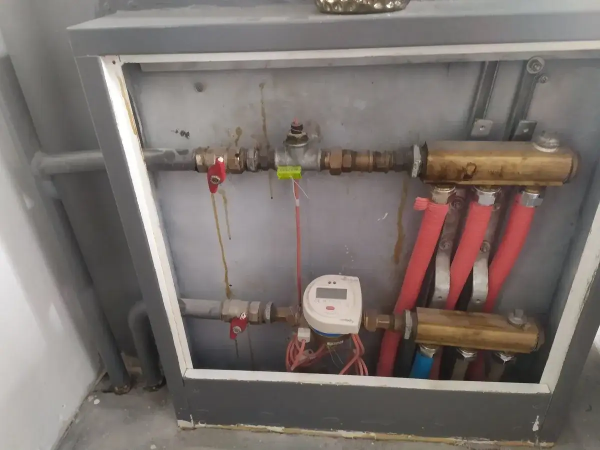 Zawory i licznik ciepła w instalacji grzewczej. Widać rury i czerwone węże, pomocne przy pytaniu jak zakręcić wodę w kaloryferze.