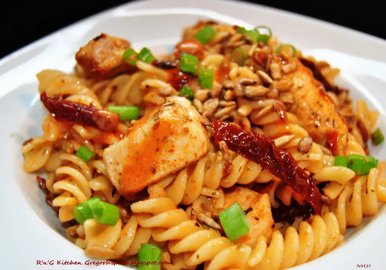 Pyszny makaron z kurczakiem, suszonymi pomidorami i pestkami słonecznika, posypany szczypiorkiem.