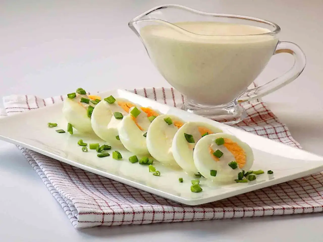 Jajka na twardo polane kremowym sosem chrzanowym, posypane szczypiorkiem. Obok sosjerka z sosem.