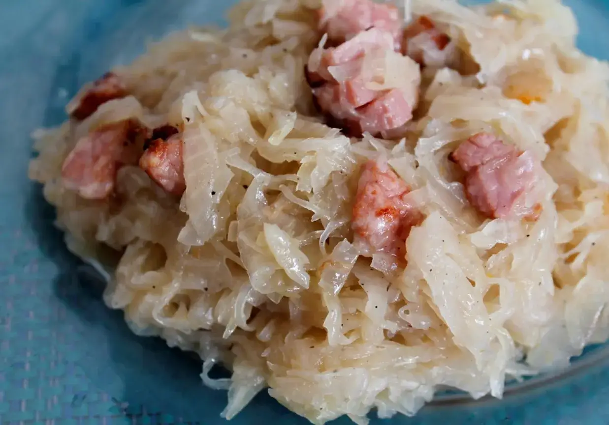 Pyszna kapusta kiszona zasmażana z kawałkami boczku, podana na niebieskim talerzu.