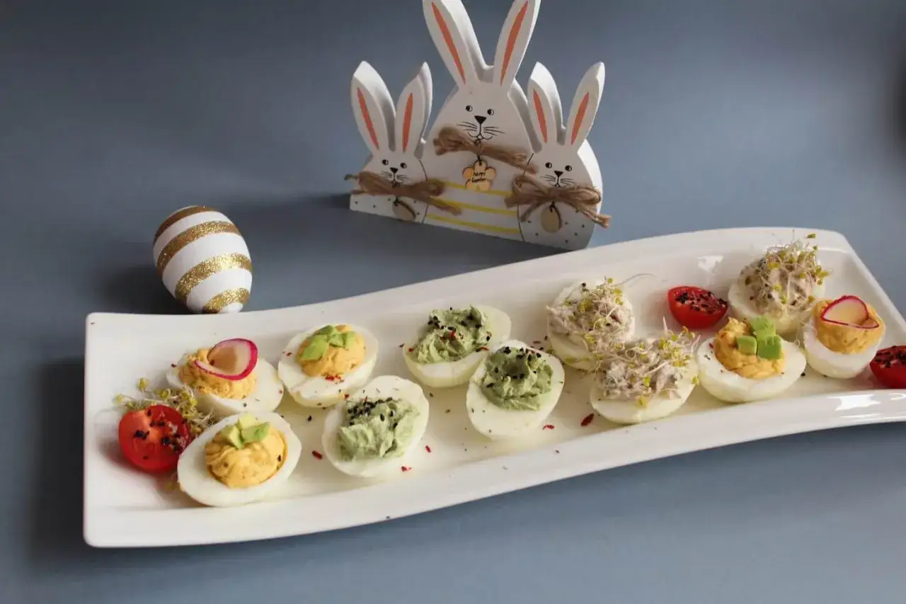 Wielkanocne jajka faszerowane na talerzu, obok ozdobne zajączki. Inspiracja na 14 przepis&oacute;w na jajka faszerowane.