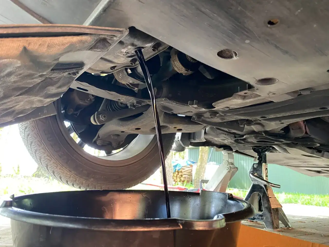 Stary olej spływa z silnika do miski. Pokazuje to, jak wymienić olej w samochodzie bez kanału, podnosząc auto na podnośniku.